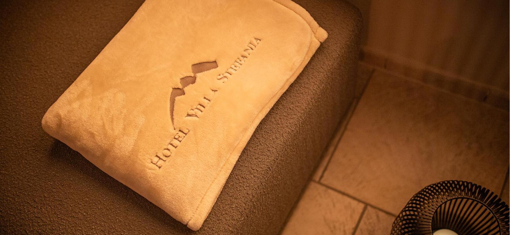 Beige Decke im Ruheraum mit dem aufgestickten Logo vom Hotel Villa Stefania.