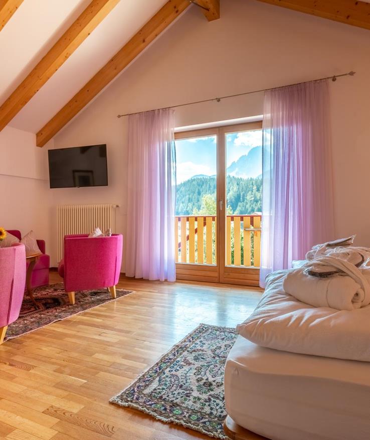 Junior Suite con letto matrimoniale, angolo soggiorno, pavimento in legno chiaro e balcone con vista sulle Dolomiti.