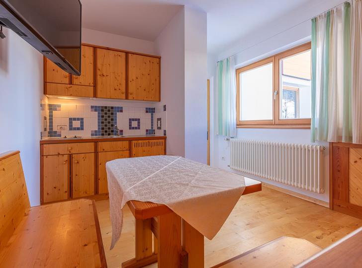 Family Suite con angolo cottura in legno chiaro, tavolo da pranzo con panca e finestra con tende chiare.