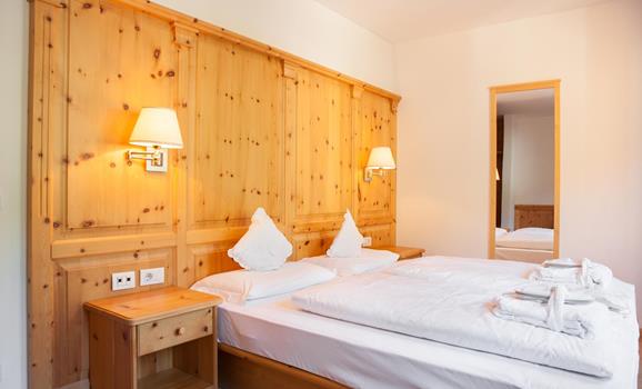 Doppelzimmer Classic mit Holzvertäfelung, breitem Bett mit weißer Bettwäsche, Wandleuchten und Blick in den Vorraum.