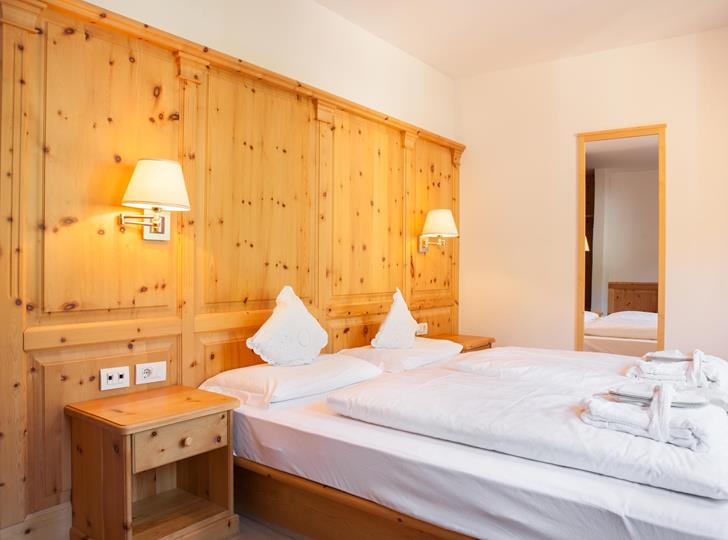 Classic double room with wood panelling, a wide bed with white linens, wall lamps and a view through to the entrance area.