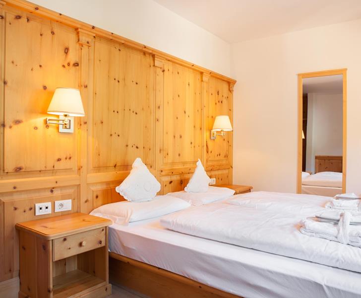 Doppelzimmer Classic mit Holzvertäfelung, breitem Bett mit weißer Bettwäsche, Wandleuchten und Blick in den Vorraum.