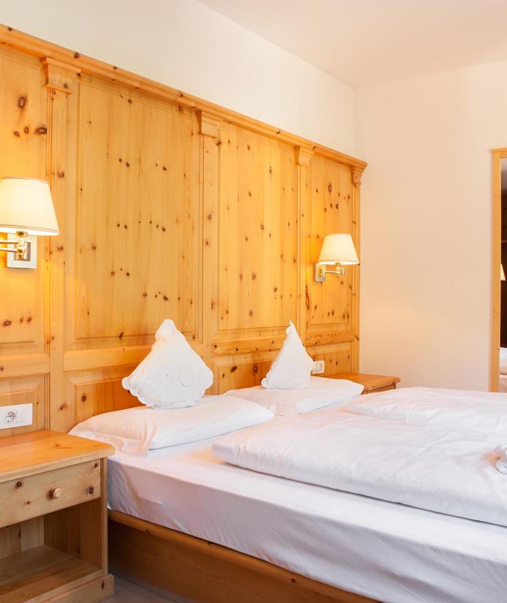 Camera doppia Classic con rivestimento in legno, letto ampio con biancheria bianca, applique e vista sull'ingresso.