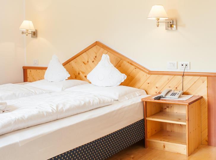 Zimmer Superior mit Doppelbett, Holzvertäfelung und Nachtkästchen.