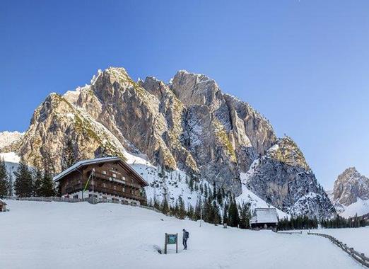 Dreischusterhütte in the Dolomites with snow-covered meadows and impressive mountains in the background.