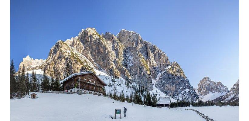 Rifugio Tre Scarperi nelle Dolomiti con prati innevati e imponenti montagne sullo sfondo.