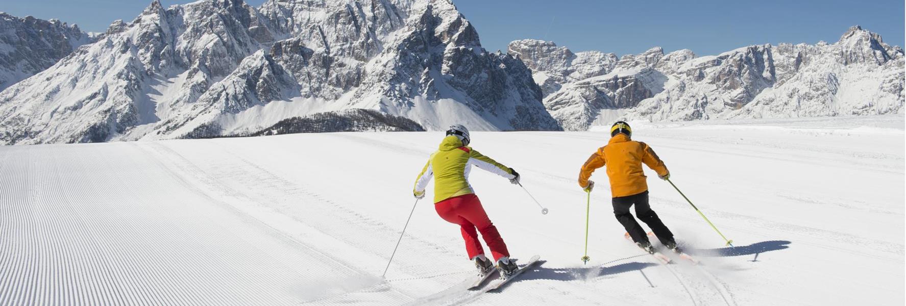 Zwei Skifahrer auf einer präparierten Skipiste in der verschneiten Berglandschaft der Dolomiten.