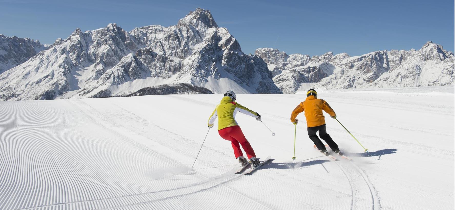 Zwei Skifahrer auf einer präparierten Skipiste in der verschneiten Berglandschaft der Dolomiten.