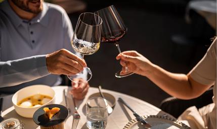 Two people toast with glasses of red wine during a meal.