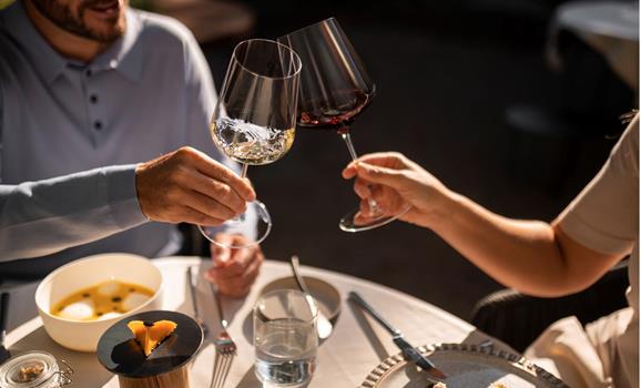 Two people toast with glasses of red wine during a meal.
