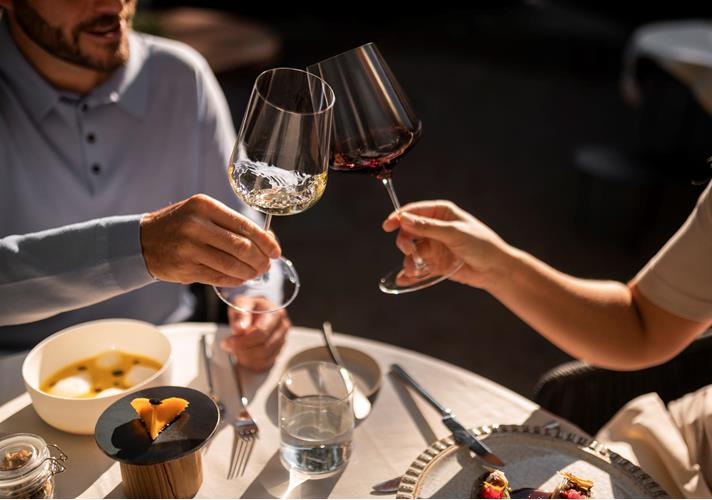 Two people toast with glasses of red wine during a meal.