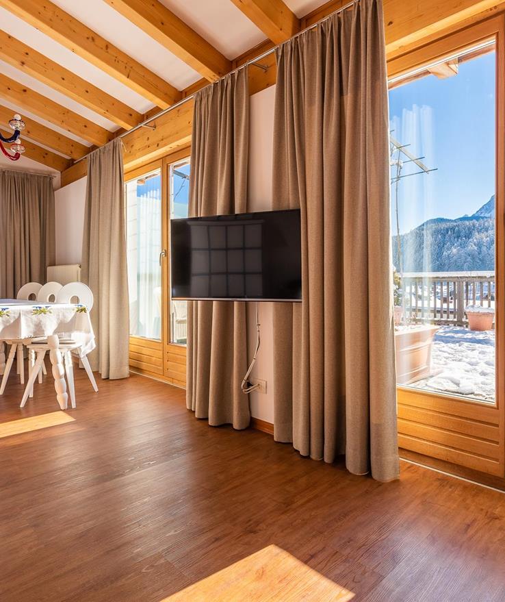 Suite Panorama con pavimento in legno, ampie finestre panoramiche, angolo relax accogliente e vista sulle Dolomiti.