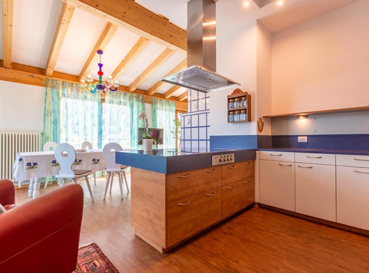 Offene Küche mit Holzbalkendecke, blauem Fliesenspiegel und Essbereich mit roten Stühlen.