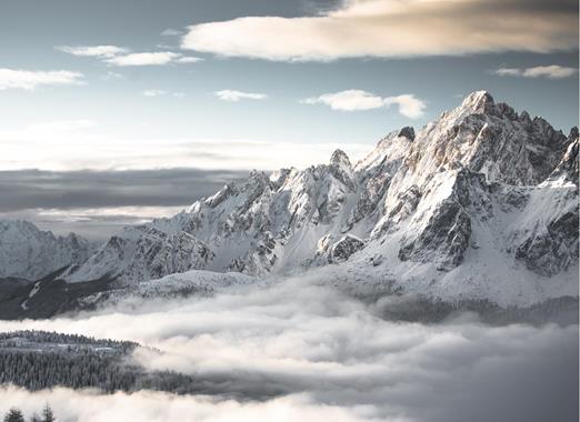 Snow-covered winter landscape in the Dolomites, with snow-capped mountain peaks and blue sky.