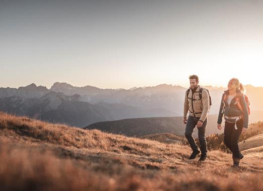 Zwei Wanderer in herbstlicher Berglandschaft mit massiven Gebirge im Hintergrund.