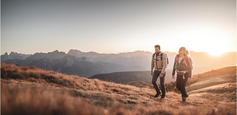 Zwei Wanderer in herbstlicher Berglandschaft mit massiven Gebirge im Hintergrund.