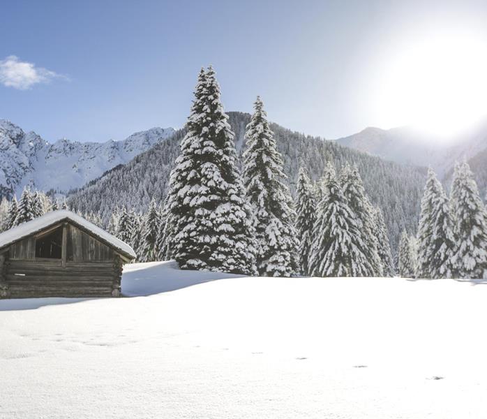 Hütte in verschneiter Winterlandschaft mit massiver Berglandschaft und blauem Himmel im Hintergrund.