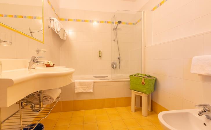 Badezimmer Family Suite mit Duschbadewanne, kleinem und großem Waschbecken mit hellen Fließen.