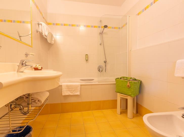 Badezimmer Family Suite mit Duschbadewanne, kleinem und großem Waschbecken mit hellen Fließen.