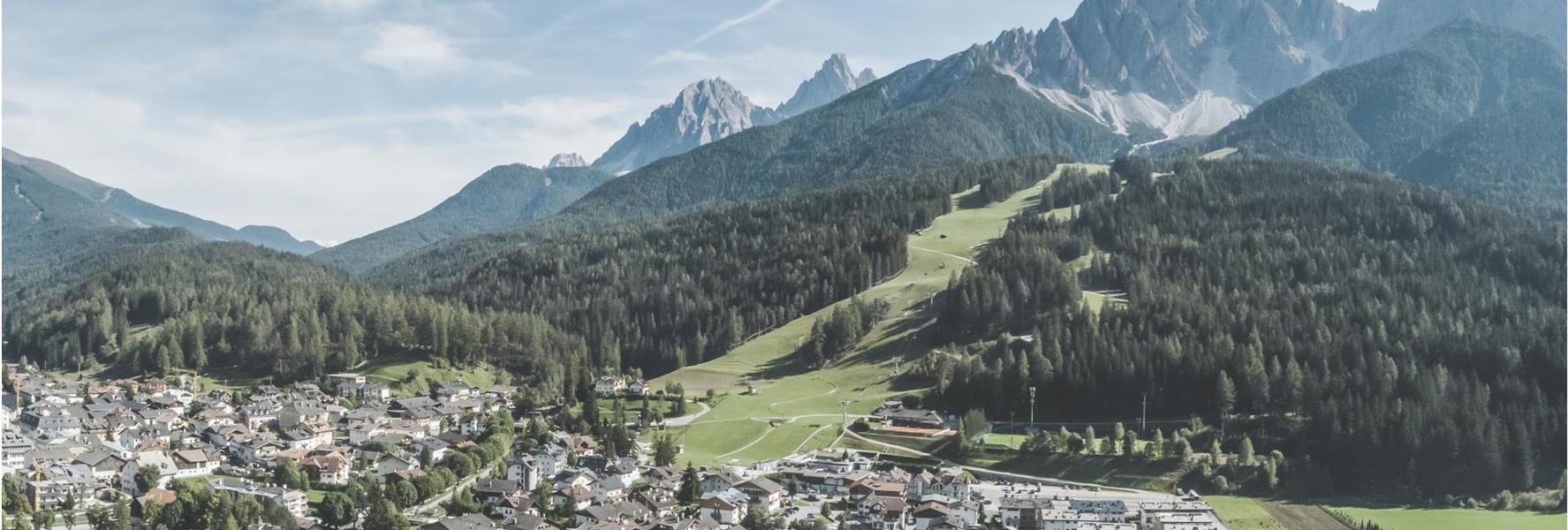 Aerial view of San Candido with meadows, forests and mountains in the background.
