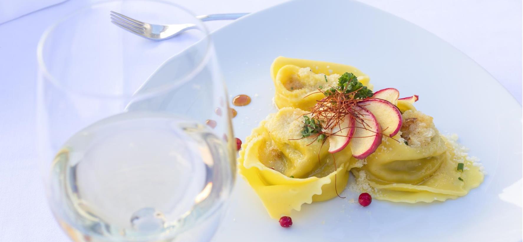 Tortellini su un piatto bianco con burro fuso, Parmigiano ed erbe aromatiche fresche.