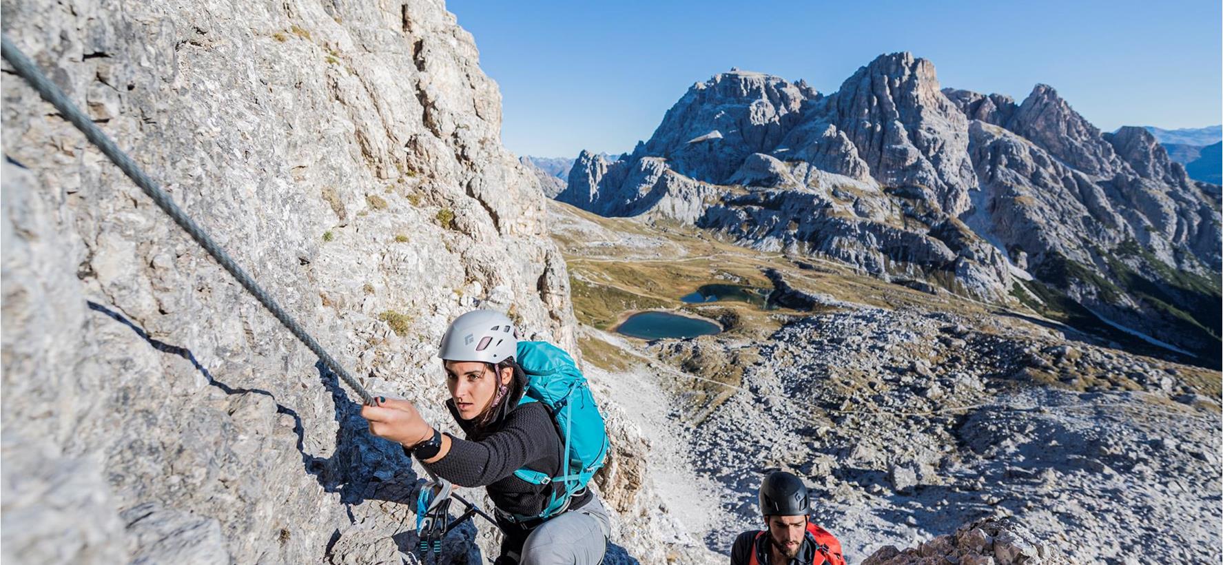 Arrampicatore su una via ferrata nelle Dolomiti, con ripide pareti rocciose e paesaggio montano sullo sfondo