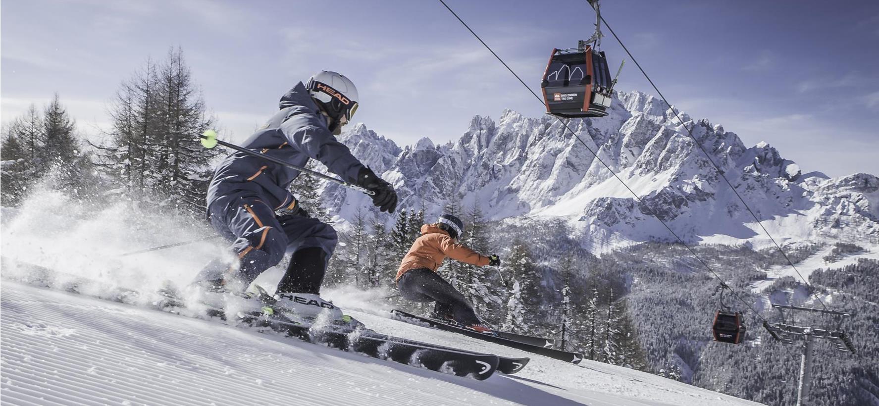 Skifahrer auf einer Skipiste in den verschneiten Dolomiten mit markanten Berggipfeln im Hintergrund.