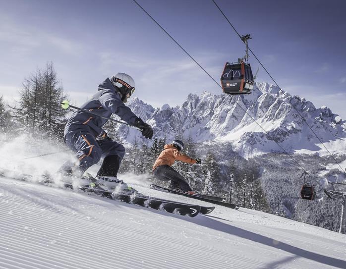 Skifahrer auf einer Skipiste in den verschneiten Dolomiten mit markanten Berggipfeln im Hintergrund.