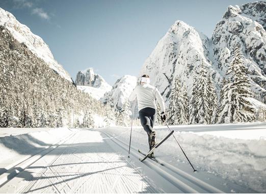 Un fondista su una pista da sci di fondo in un paesaggio invernale con alberi innevati e montagne sullo sfondo.