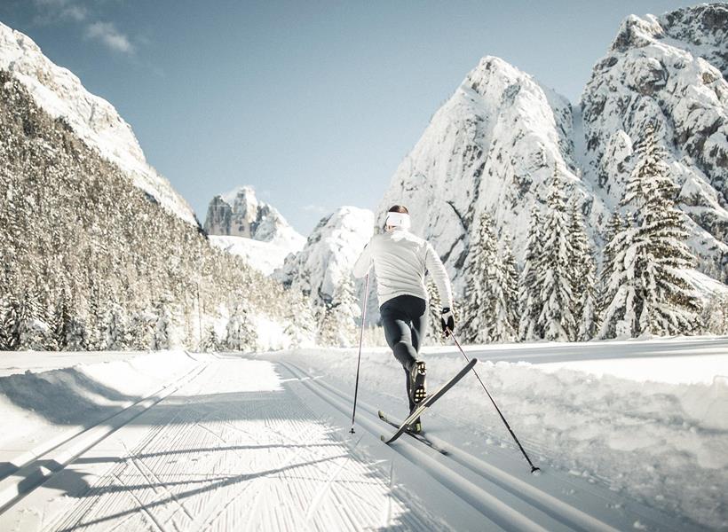 A cross-country skier on a trail in a winter landscape with snow-covered trees and mountains in the background.