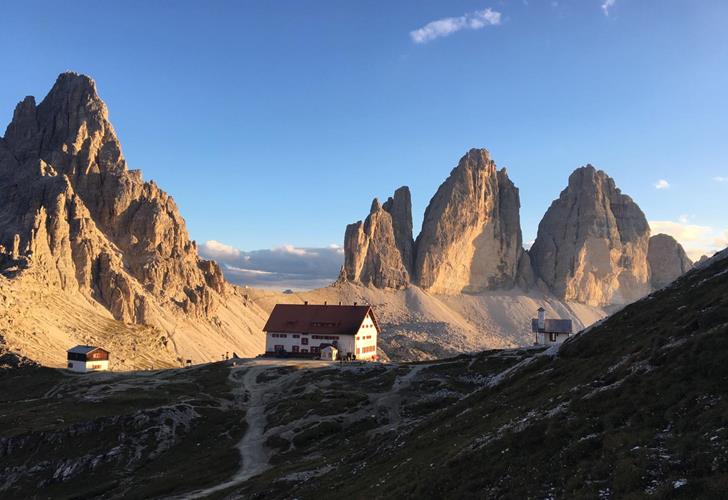 Goldenes Morgenlicht über den Drei Zinnen in den Dolomiten mit markanten Felsformationen und alpiner Berglandschaft.