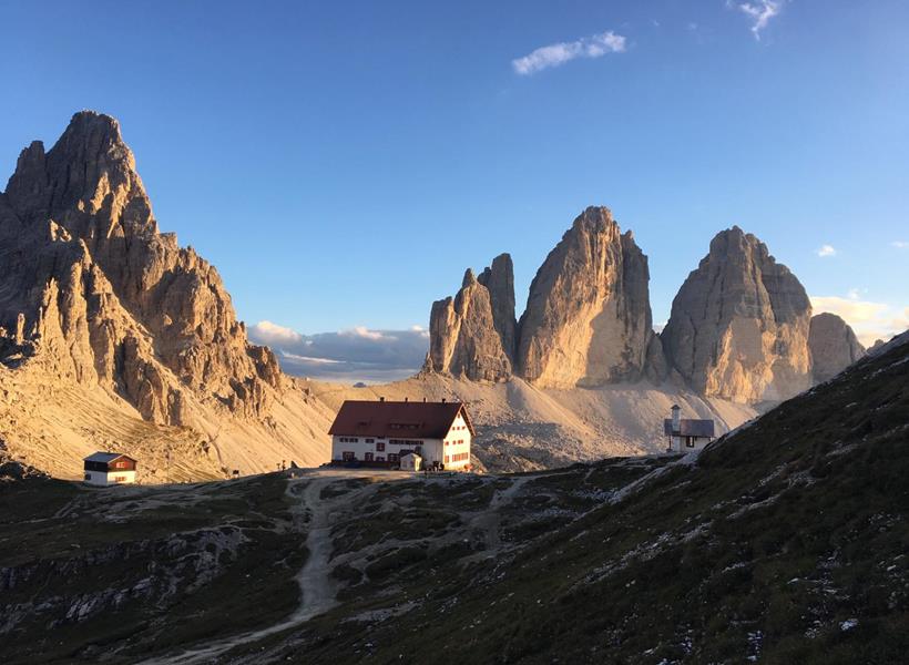 Goldenes Morgenlicht über den Drei Zinnen in den Dolomiten mit markanten Felsformationen und alpiner Berglandschaft.