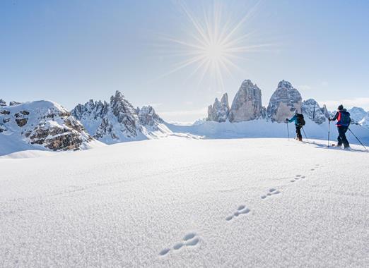 Schneeschuhwanderer in schneebedeckter Landschaft mit den markanten Dolomiten im Hintergrund.