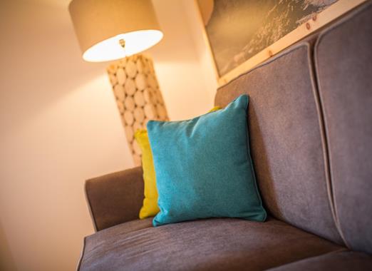 Angolo relax accogliente con divano grigio, cuscino turchese, illuminazione calda e decorazioni murali.