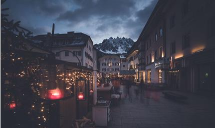Abendlicher Platz in den Dolomiten mit beleuchteten Häusern, Bergkulisse und stimmungsvoller Atmosphäre.