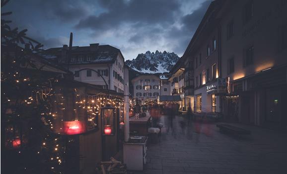 Abendlicher Platz in den Dolomiten mit beleuchteten Häusern, Bergkulisse und stimmungsvoller Atmosphäre.
