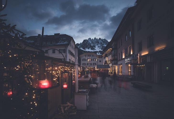 Abendlicher Platz in den Dolomiten mit beleuchteten Häusern, Bergkulisse und stimmungsvoller Atmosphäre.