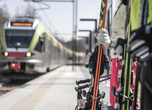 Skifahrer auf einem Bahnsteig, die ihre Ski halten und auf den einfahrenden Zug warten.