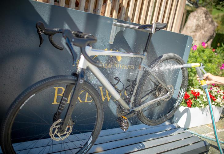 Nahaufnahme eines Fahrradds das mit einem Wasserschlauch abgespritzt wird.