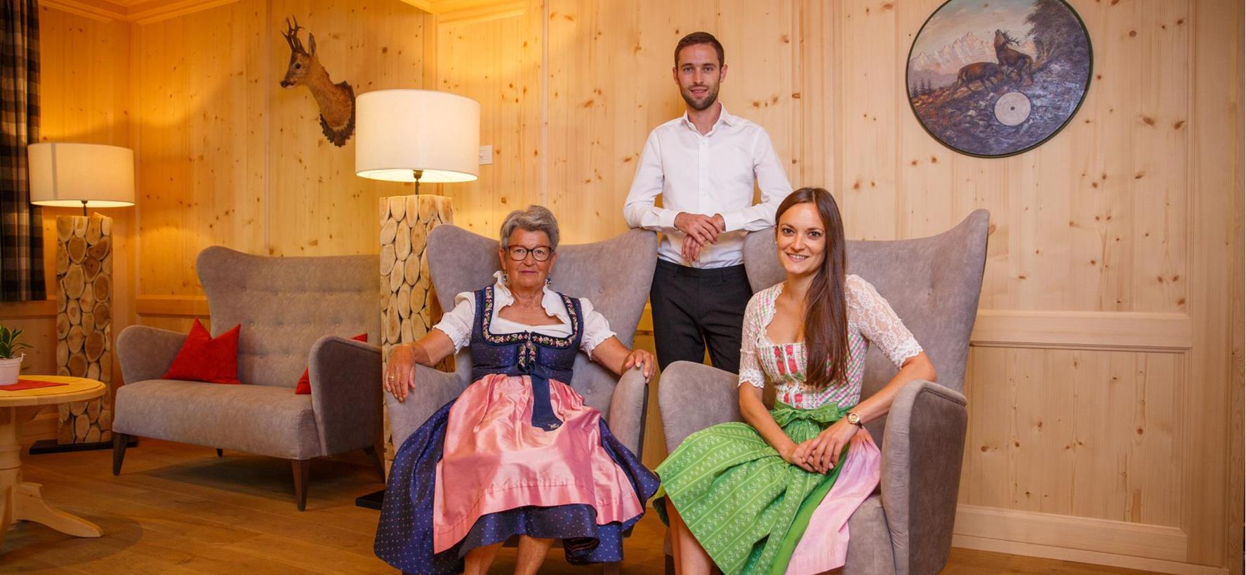 Familie Ortner sitzen auf grauen Sesseln in einer hellen mit holzgetäfelten Stube
