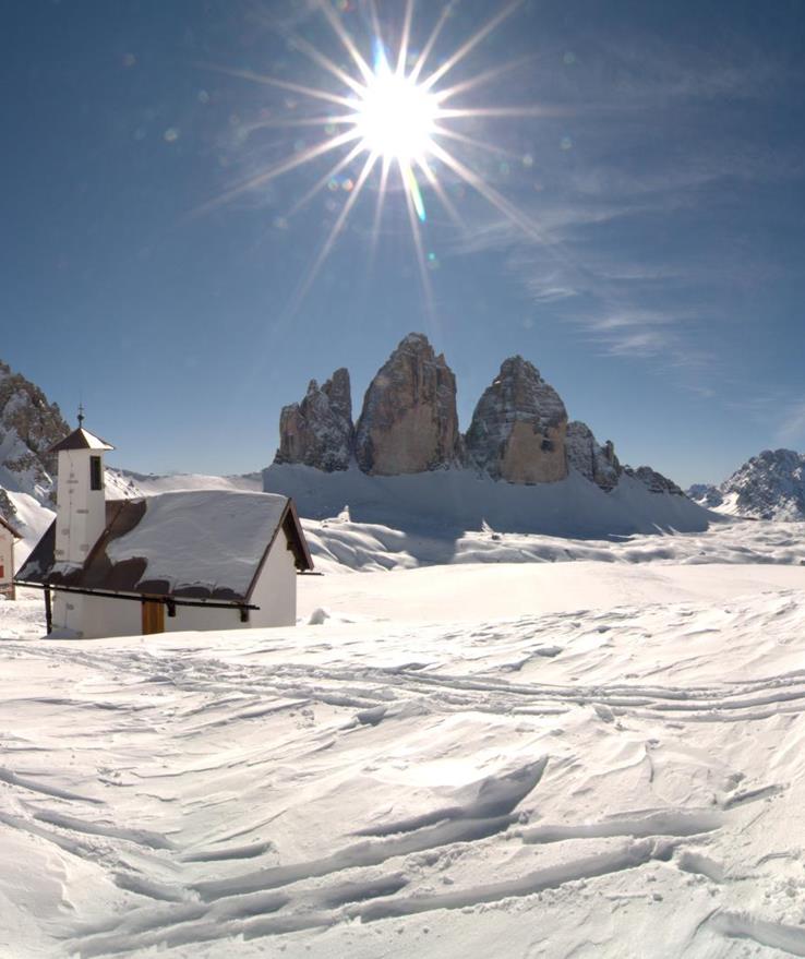Snow-covered Tre Cime di Lavaredo in the Dolomites under a blue winter sky.