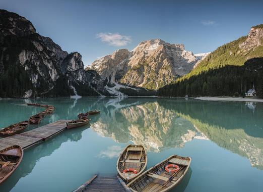 Lake Braies with rowing boats on the water, the small chapel and the surrounding mountain landscape.
