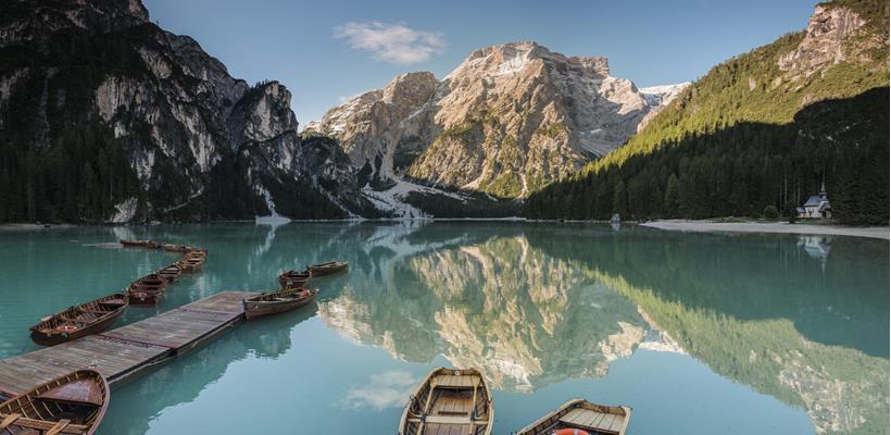 Lake Braies with rowing boats on the water, the small chapel and the surrounding mountain landscape.