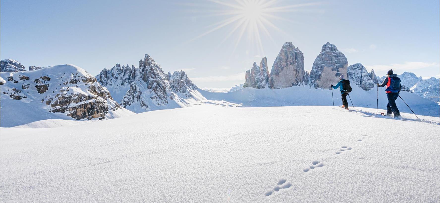 Escursionisti con le ciaspole in un paesaggio innevato con le imponenti Dolomiti sullo sfondo.