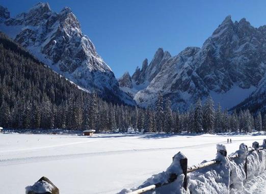 Snow-covered Fischleintal valley with coniferous forest and distinctive Dolomite peaks in the background.