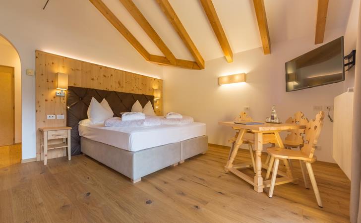 Bright double room in the Suite Natura with wooden flooring, exposed ceiling beams and a small seating area.