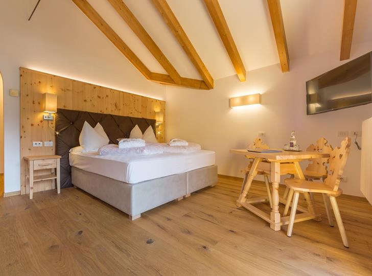 Helles Doppelzimmer Suite Natura mit Holzboden, sichtbaren Deckenbalken und kleiner Sitzecke.