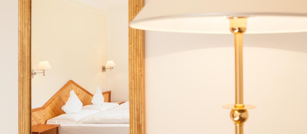 Lampada da terra accanto a uno specchio con vista sul letto matrimoniale della camera.