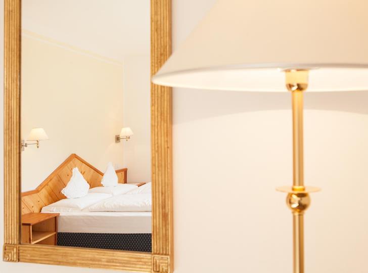 Stehlampe neben einem Spiegel mit Blick auf das Doppelbett im Zimmer.