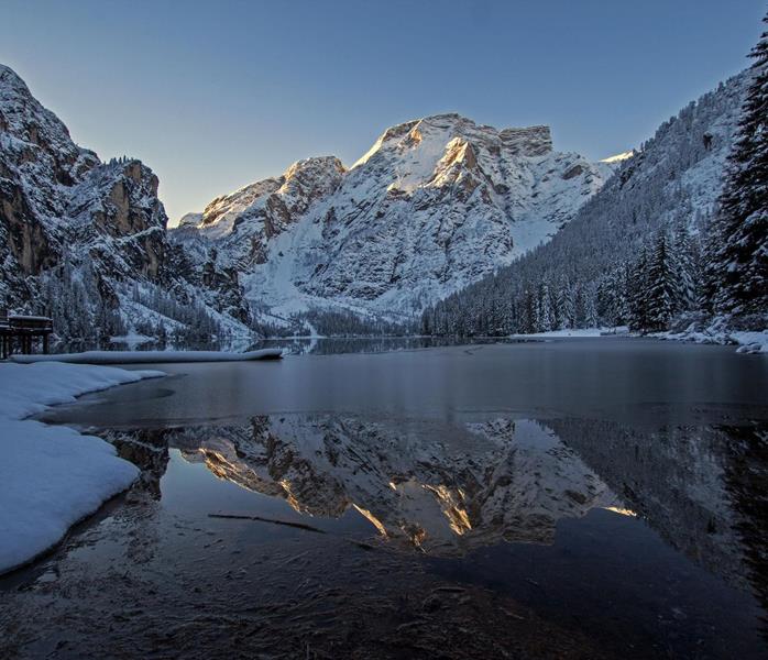 Pragser Wildsee im Winter mit zugefrorenem See, schneebedeckten Bäumen und Bergen im Hintergrund.
